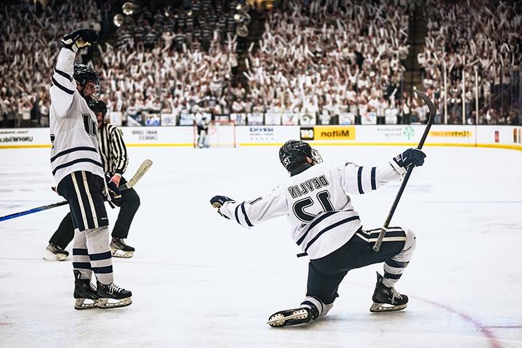 A UNH hockey player celebrates a goal in front of excited fans